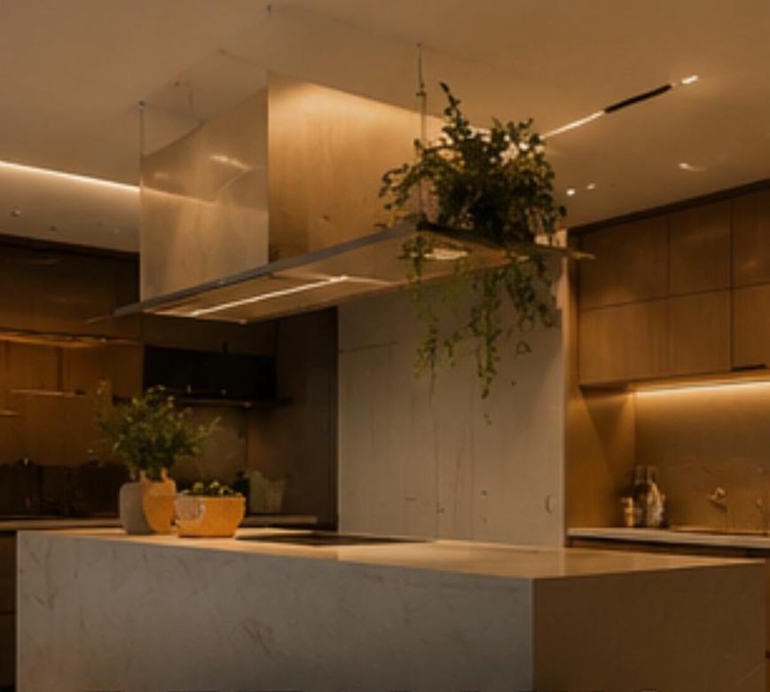 Cozinha sofisticada com ilha de mármore, coifa suspensa com planta pendente e marcenaria em madeira sob iluminação quente, projeto D'Lócus